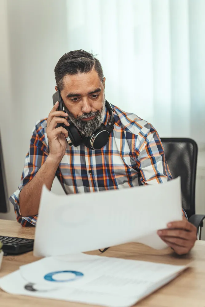 Man on the phone, reviewing documents, likely related to real estate bookkeeping
