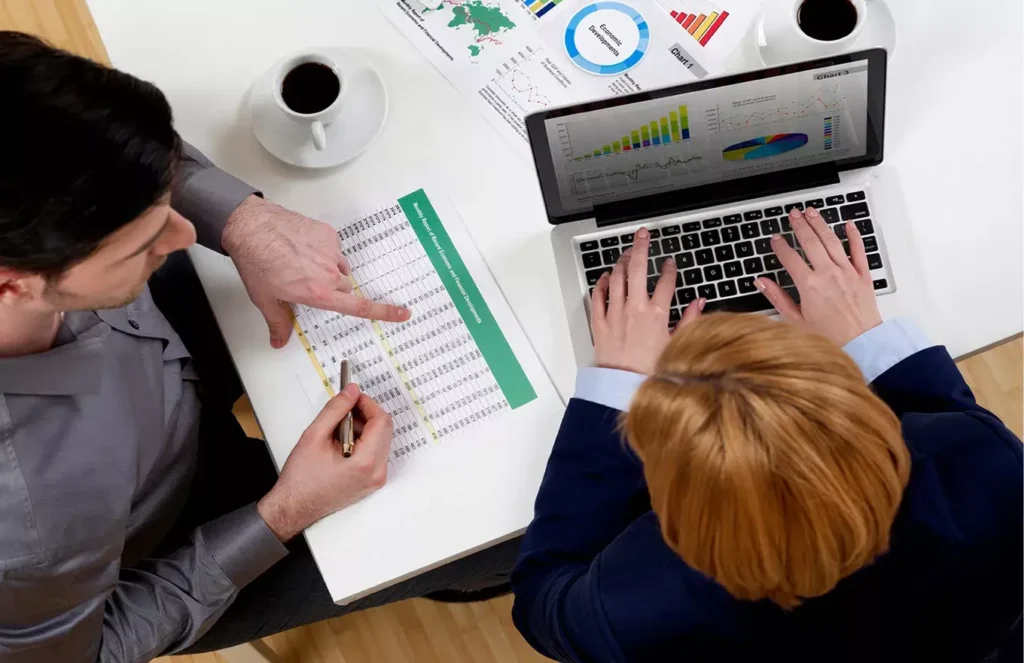 Business team analyzing financial data charts on a laptop and printed reports.