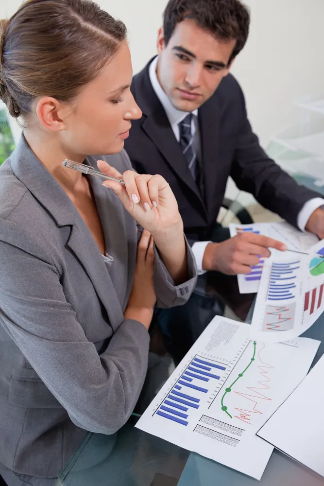 Two professionals analyzing financial charts and graphs at a glass office table